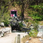 Locals bathing in a spring below a pink roadside shrine